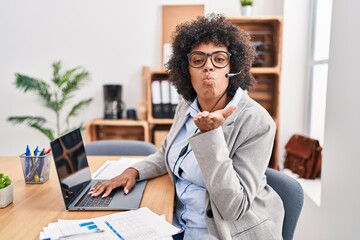 Poster - Black woman with curly hair wearing call center agent headset at the office looking at the camera blowing a kiss with hand on air being lovely and sexy. love expression.