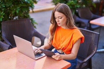 Canvas Print - Young woman using laptop and touchpad sitting on table at coffee shop terrace