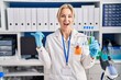 © Krakenimages.com - Young caucasian woman working at scientist laboratory holding test tubes pointing thumb up to the side smiling happy with open mouth