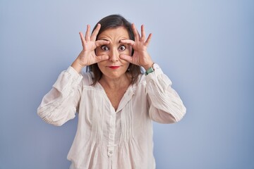 Canvas Print - Middle age hispanic woman standing over blue background trying to open eyes with fingers, sleepy and tired for morning fatigue