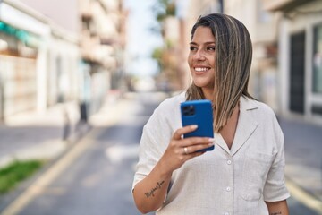 Poster - Young hispanic woman smiling confident using smartphone at street