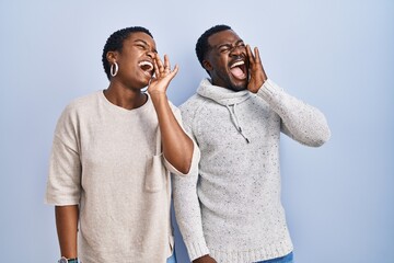 Canvas Print - Young african american couple standing over blue background together shouting and screaming loud to side with hand on mouth. communication concept.