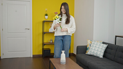 Poster - Young beautiful hispanic woman putting flowers on pot at home