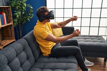 Sticker - Young hispanic man playing video game using virtual reality glasses at home