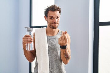 Poster - Young hispanic man wearing sportswear drinking water doing money gesture with hands, asking for salary payment, millionaire business