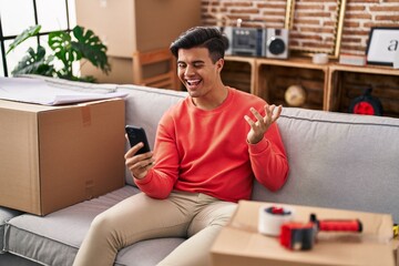 Poster - Hispanic man moving to a new home doing video call with smartphone celebrating achievement with happy smile and winner expression with raised hand