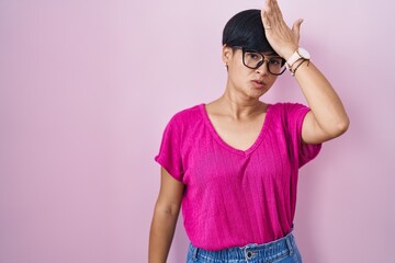 Poster - Young asian woman with short hair standing over pink background surprised with hand on head for mistake, remember error. forgot, bad memory concept.