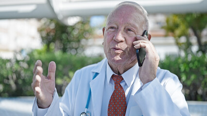 Poster - Senior grey-haired man doctor smiling confident talking on smartphone at park