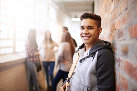Education, smile and portrait of man in college hallway for studying, learning and scholarship. Future, happy and knowledge with student relax on brick wall for university, academy and campus