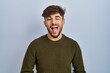 Arab man with beard standing over blue background sticking tongue out happy with funny expression. emotion concept.