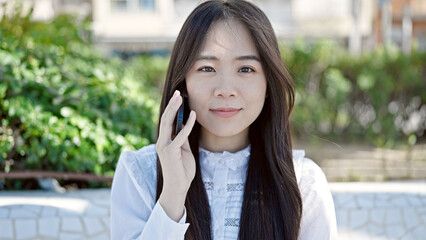 Canvas Print - Young chinese woman talking on smartphone with serious expression at park