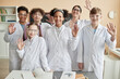 © Seventyfour - Diverse group of happy teenagers wearing lab coats in school and waving at camera standing together