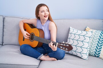 Poster - Young redhead woman playing classical guitar sitting on sofa at home