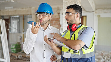 Sticker - Two men builders and architect writing on document sending voice message by smartphone at construction site