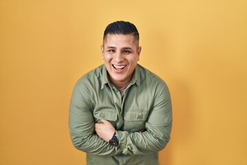 Canvas Print - Hispanic young man standing over yellow background smiling and laughing hard out loud because funny crazy joke with hands on body.