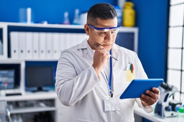 Canvas Print - Young latin man scientist using touchpad with doubt expression at laboratory