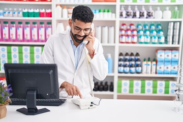 Sticker - Young arab man pharmacist talking on telephone using computer at pharmacy