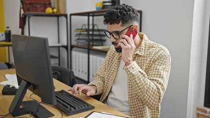 Sticker - Young hispanic man business worker using computer talking on smartphone at office