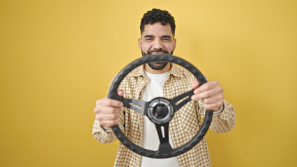 Sticker - Young hispanic man smiling confident using steering wheel as a driver over isolated yellow background