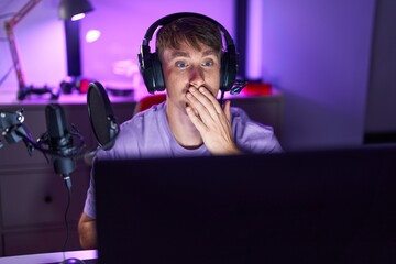 Sticker - Caucasian blond man playing video games covering mouth with hand, shocked and afraid for mistake. surprised expression