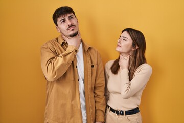 Wall Mural - Young hispanic couple standing over yellow background touching painful neck, sore throat for flu, clod and infection