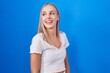 © Krakenimages.com - Young caucasian woman standing over blue background looking away to side with smile on face, natural expression. laughing confident.