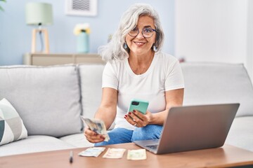 Poster - Middle age woman accounting using laptop and smartphone sitting on sofa at home