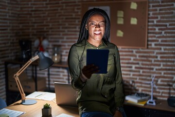 Wall Mural - Young african american with braids working at the office at night winking looking at the camera with sexy expression, cheerful and happy face.