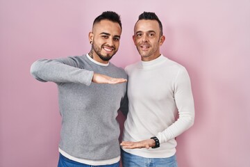 Poster - Homosexual couple standing over pink background gesturing with hands showing big and large size sign, measure symbol. smiling looking at the camera. measuring concept.