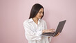 © Krakenimages.com - Young beautiful hispanic woman smiling confident using laptop over isolated pink background