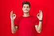 © Krakenimages.com - Young hispanic man standing over red background relaxed and smiling with eyes closed doing meditation gesture with fingers. yoga concept.