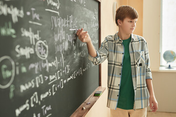 side view portrait of teen schoolboy answering in class by blackboard, copy space
