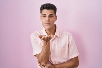 Poster - Young hispanic man standing over pink background looking at the camera blowing a kiss with hand on air being lovely and sexy. love expression.