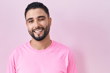 Sticker - Hispanic young man standing over pink background winking looking at the camera with sexy expression, cheerful and happy face.