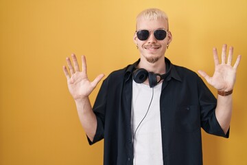 Sticker - Young caucasian man wearing sunglasses standing over yellow background showing and pointing up with fingers number ten while smiling confident and happy.