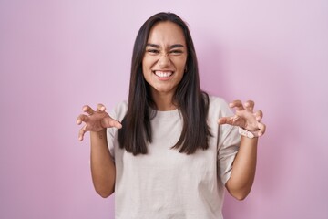 Wall Mural - Young hispanic woman standing over pink background smiling funny doing claw gesture as cat, aggressive and sexy expression