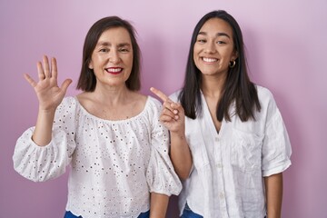 Wall Mural - Hispanic mother and daughter together showing and pointing up with fingers number six while smiling confident and happy.