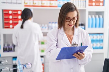 Poster - Two women pharmacist smiling confident writing on document at pharmacy