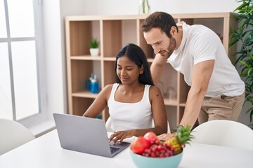 Canvas Print - Man and woman interracial couple using laptop sitting on table at home