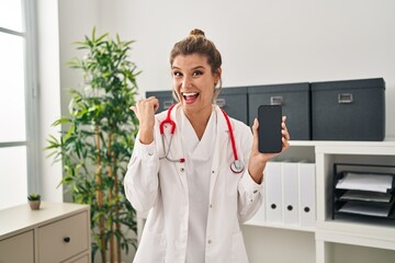 Sticker - Young woman wearing doctor uniform holding smartphone pointing thumb up to the side smiling happy with open mouth