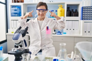 Poster - Hispanic girl with down syndrome working at scientist laboratory smiling pointing to head with both hands finger, great idea or thought, good memory