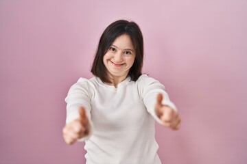 Canvas Print - Woman with down syndrome standing over pink background approving doing positive gesture with hand, thumbs up smiling and happy for success. winner gesture.