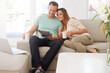 © Alexandra W/peopleimages.com - Reading, newspaper and mature couple on couch with tea, love and affection and relax together for holiday or news. Happy partner, woman or people on sofa with morning paper in lounge and coffee