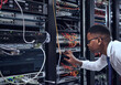 © Katleho Seisa/peopleimages.com - Black man, IT technician and server room for cyber security, data or network storage inspection. African male person or networking administrator checking system, cables or installation at datacenter