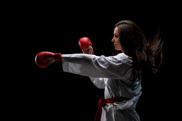 Wall Mural - girl exercising karate punch wearing kimono and red gloves against black background