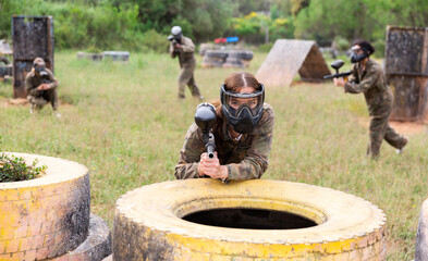 Wall Mural - Female paintball player in protective mask with ammunition and gun on paintball field