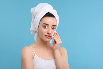 Wall Mural - Beautiful woman in terry towel removing makeup with cotton pad on light blue background, space for text