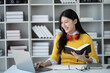 © PaeGAG - Happy young Asian woman working while reading book in the study room.