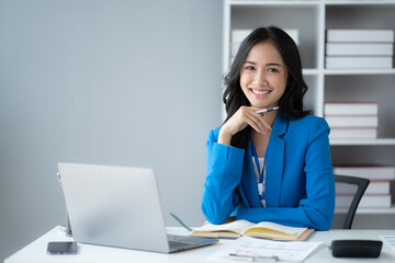 Young and pretty businesswoman sitting at her office desk, working on her project with laptop computer with positive energy.
