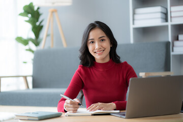 beautiful Asian girl wearing red sweater working with laptop computer in the living room.